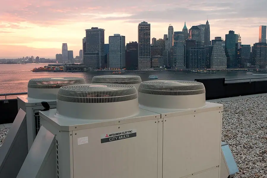 Rooftop condenser units at dusk above the city skyline